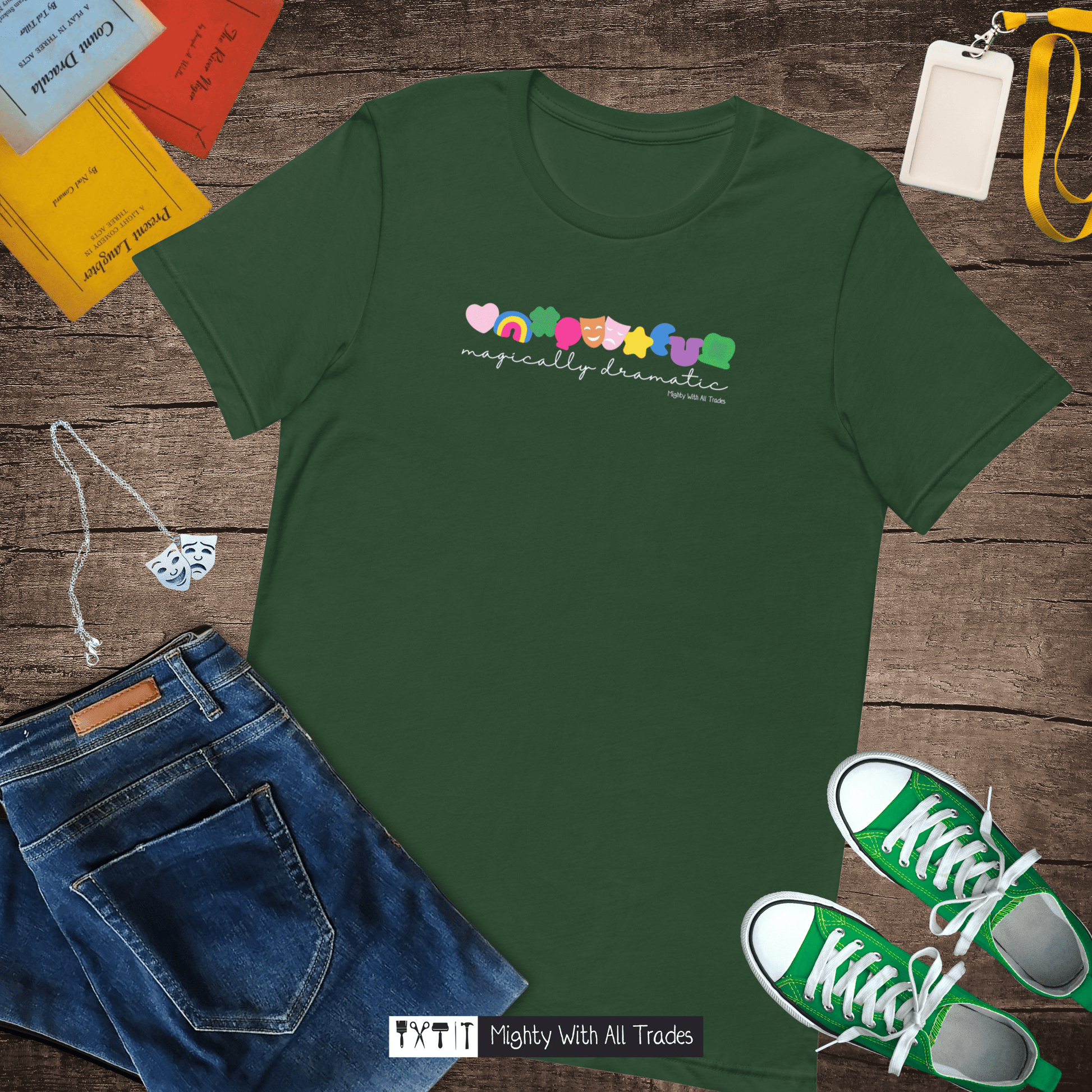 Green t-shirt with colorful text and marshmallow charm design on a wooden surface with jeans and sneakers.