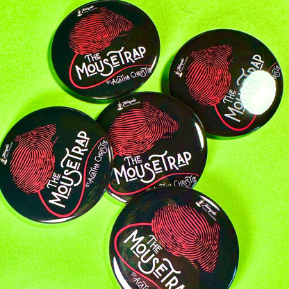 Five 'The Mousetrap' buttons by Agatha Christie on a green background
