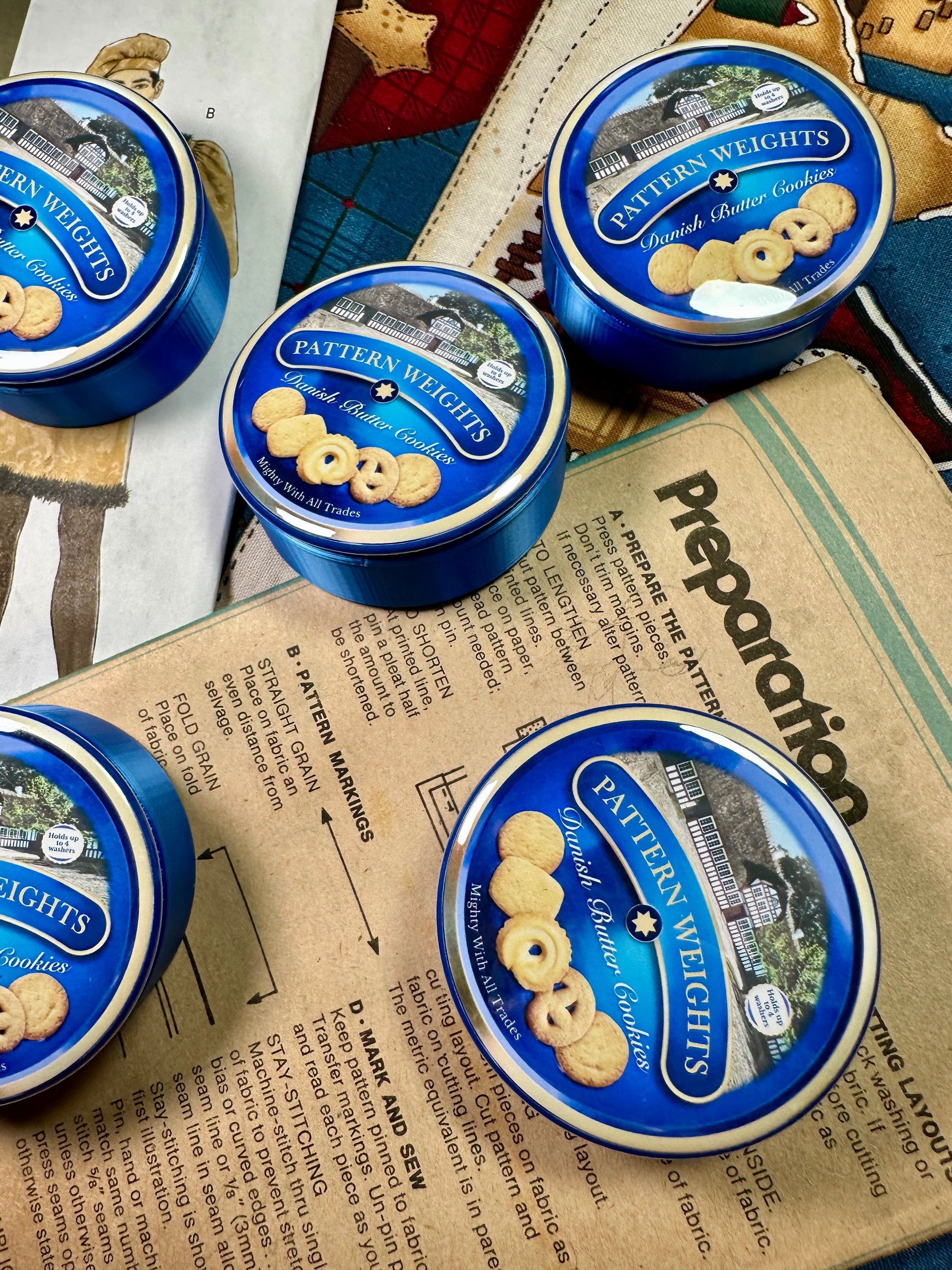 Blue tins of Pattern Weights cookies on a newspaper background