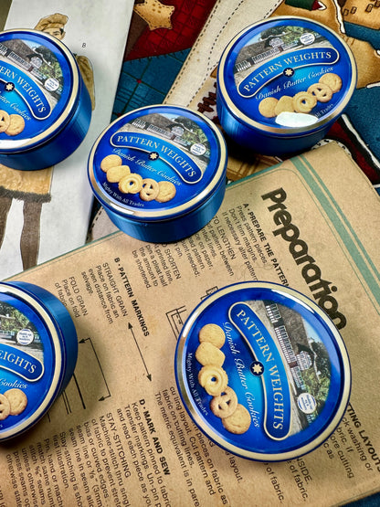Blue tins of Pattern Weights cookies on a newspaper background