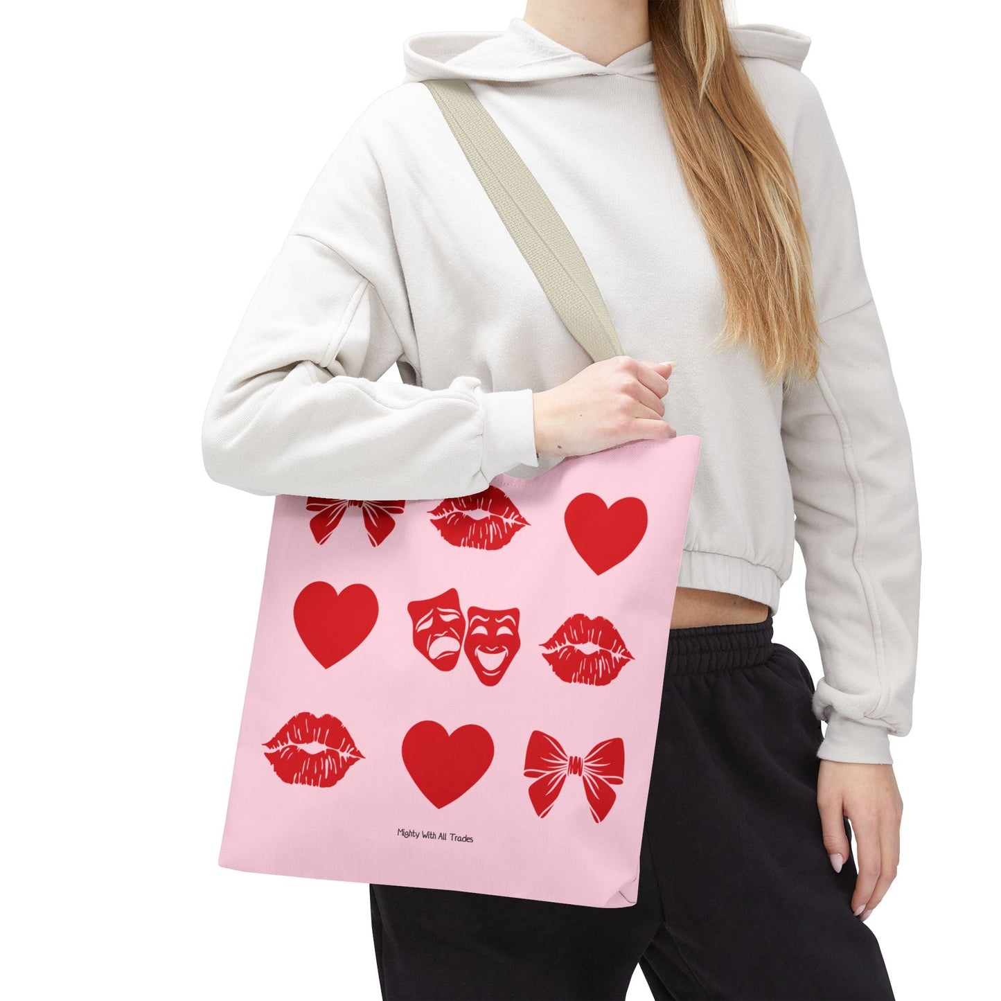 Person wearing a light gray hoodie with a pink tote bag featuring red heart, bow, theatre masks and kiss designs.