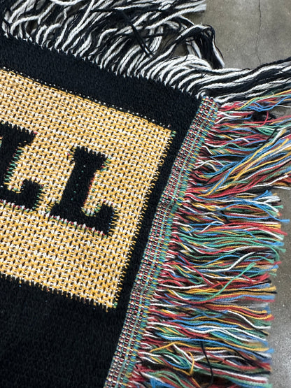 Close-up of a woven bag with colorful fringe and a visible brand logo.