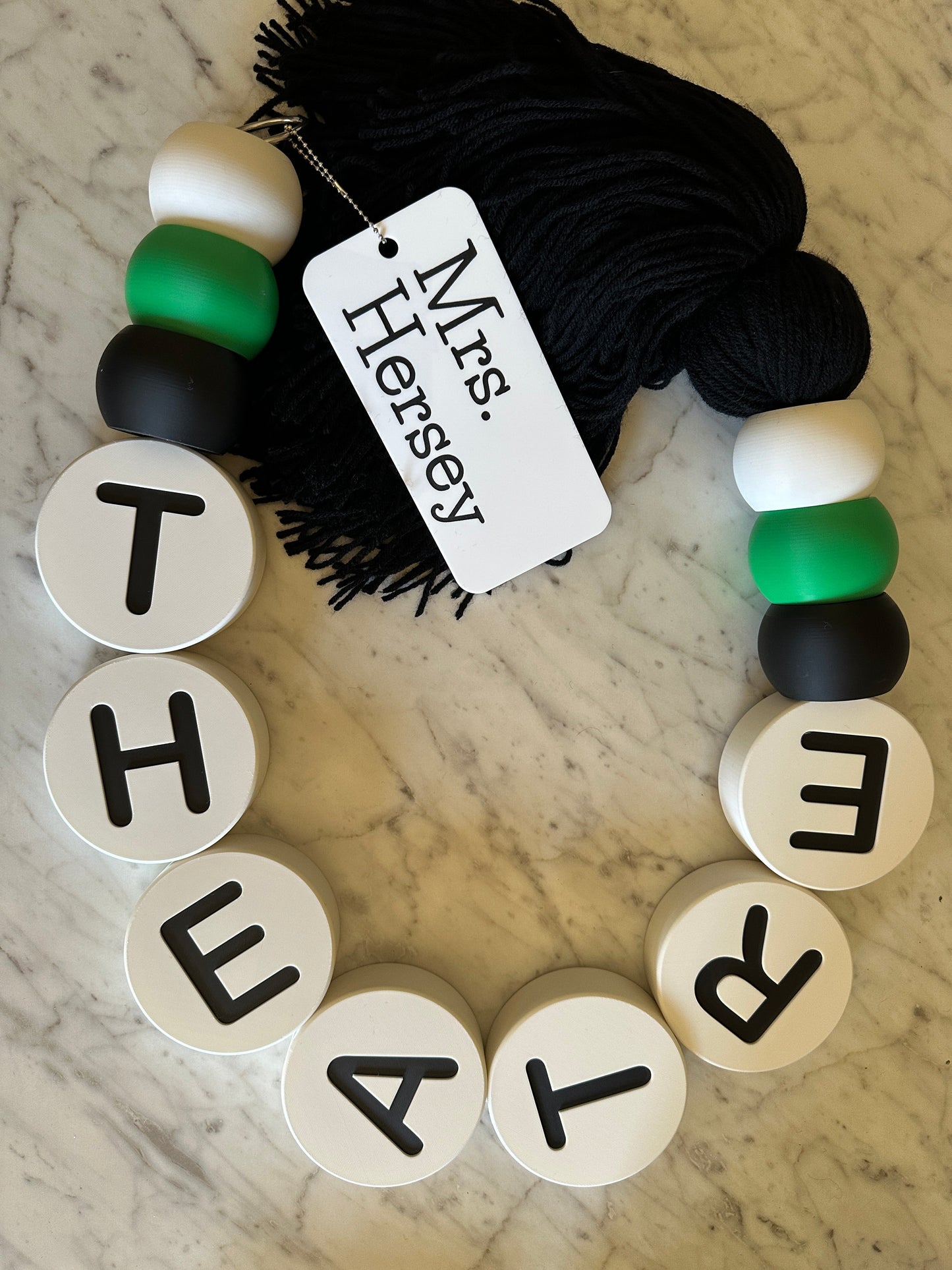 Bracelet with letter beads spelling 'THEATRE' and a tag on a marble surface.