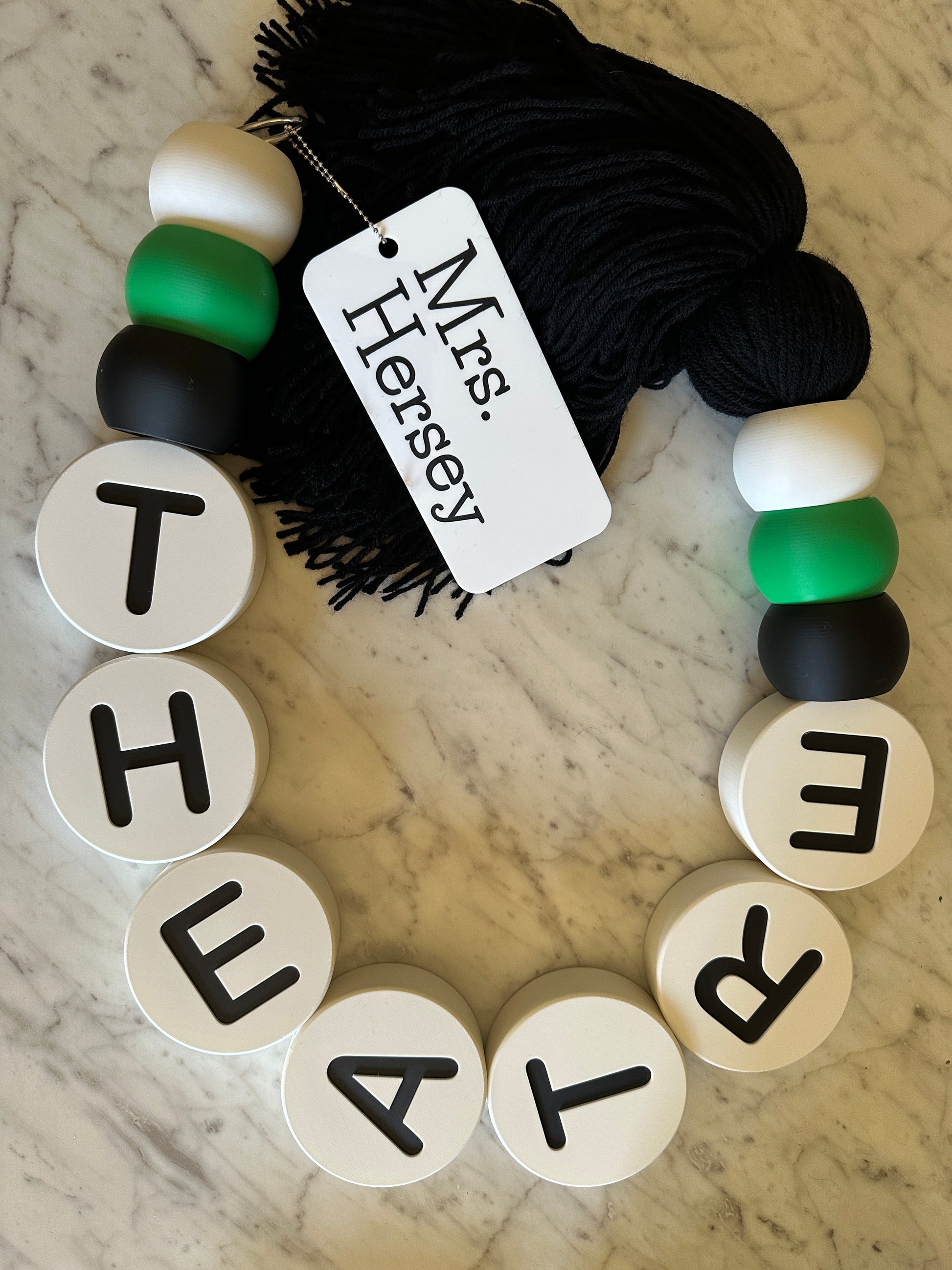 Bracelet with letter beads spelling 'THEATRE' and a tag on a marble surface.