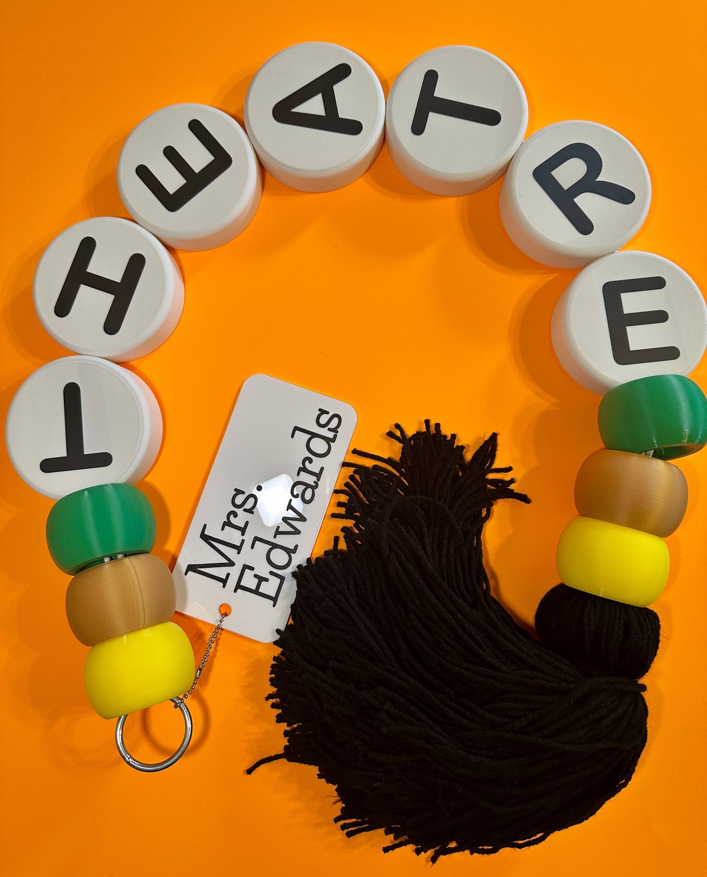 Letter beads spelling 'THEATRE' with yarn and a tag on an orange background