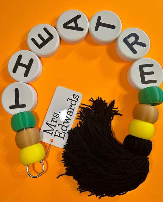 Letter beads spelling 'THEATRE' with yarn and a tag on an orange background