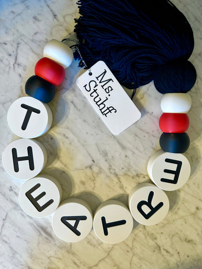 Bracelet with letter beads spelling 'THEATRE' on a marble surface with yarn.
