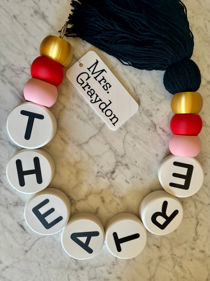 Personalized keychain with beads spelling 'THEATRE' on a marble surface.