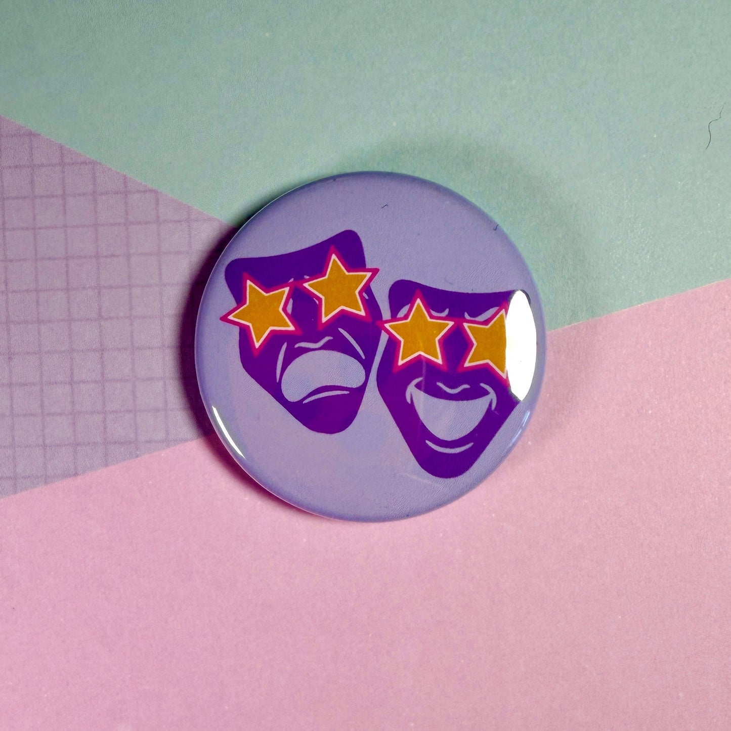 Button badge with purple masks and yellow stars on a pink and green background