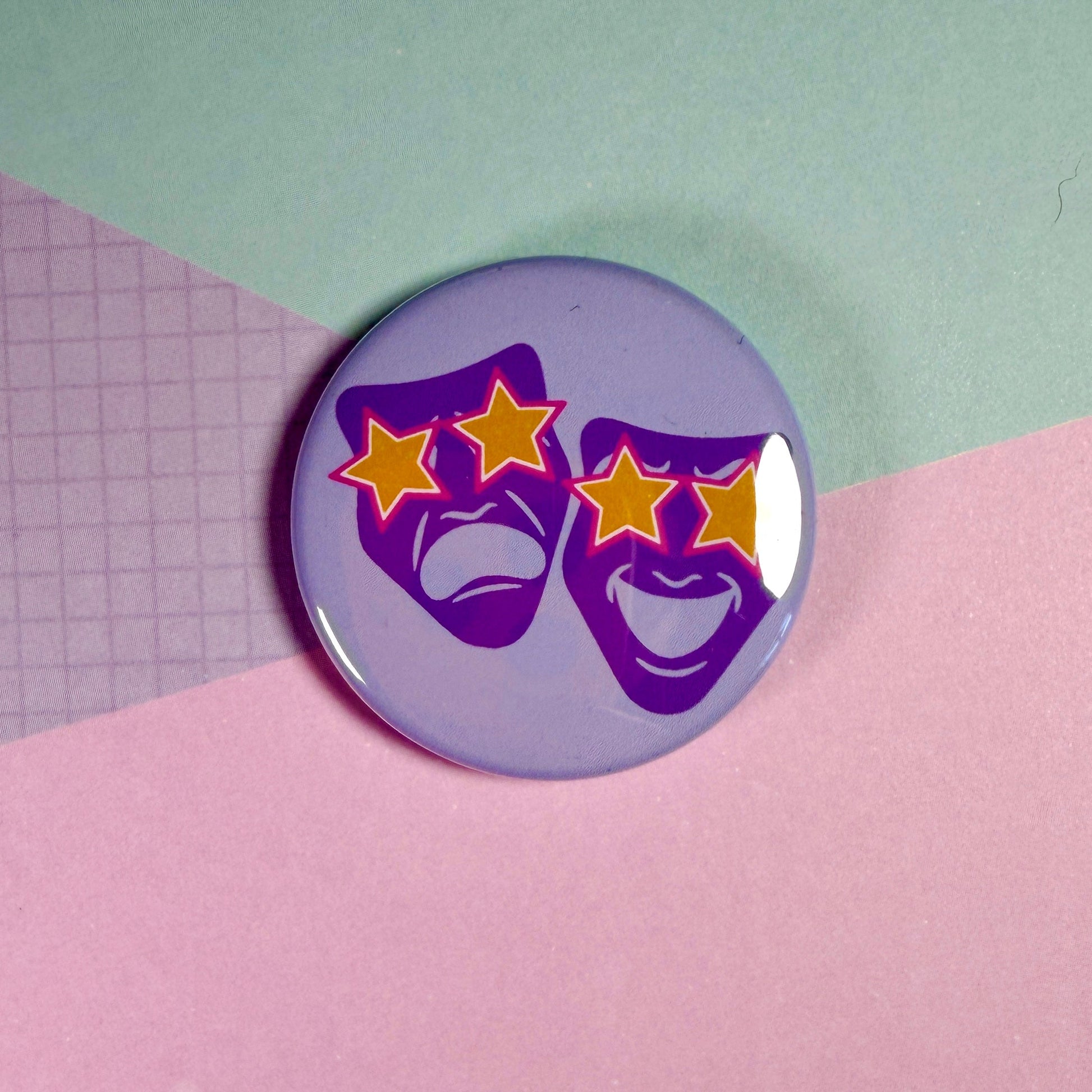 Button badge with purple masks and yellow stars on a pink and green background