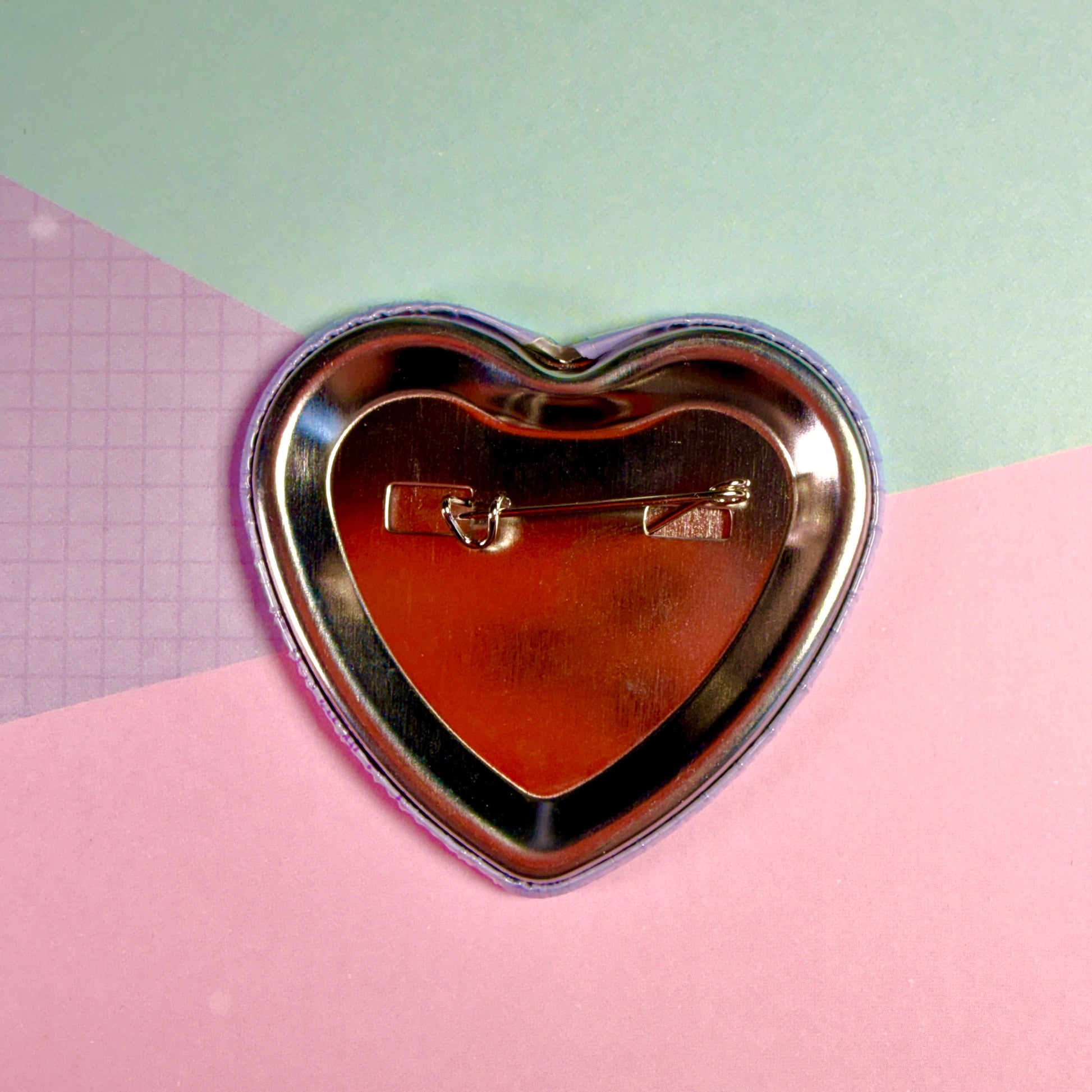 Heart-shaped metal brooch on a pink and green background