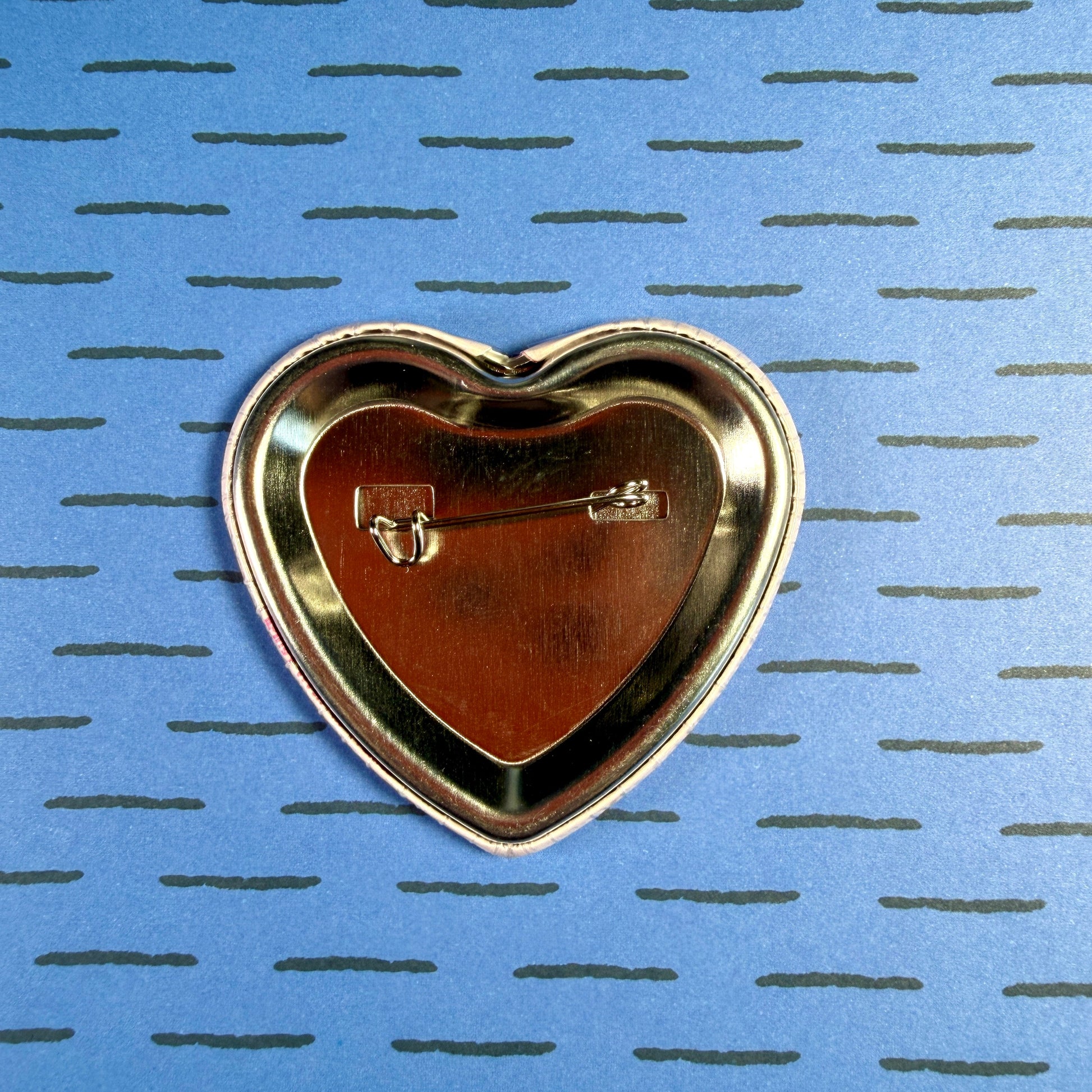 Heart-shaped gold pin on a blue background with a subtle pattern